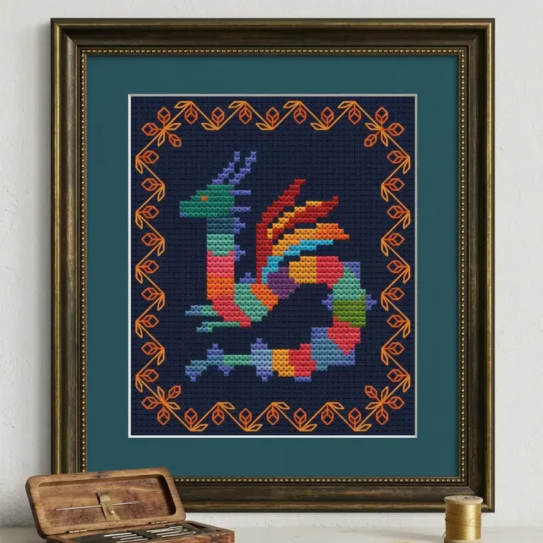 Framed cross stitch of a striped dragon with an orange border on black Aida.